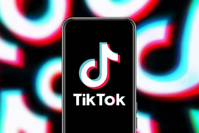A smartphone displaying the TikTok logo on its screen is set against a blurred background of the same logo, hinting at the potential to make money on TikTok.