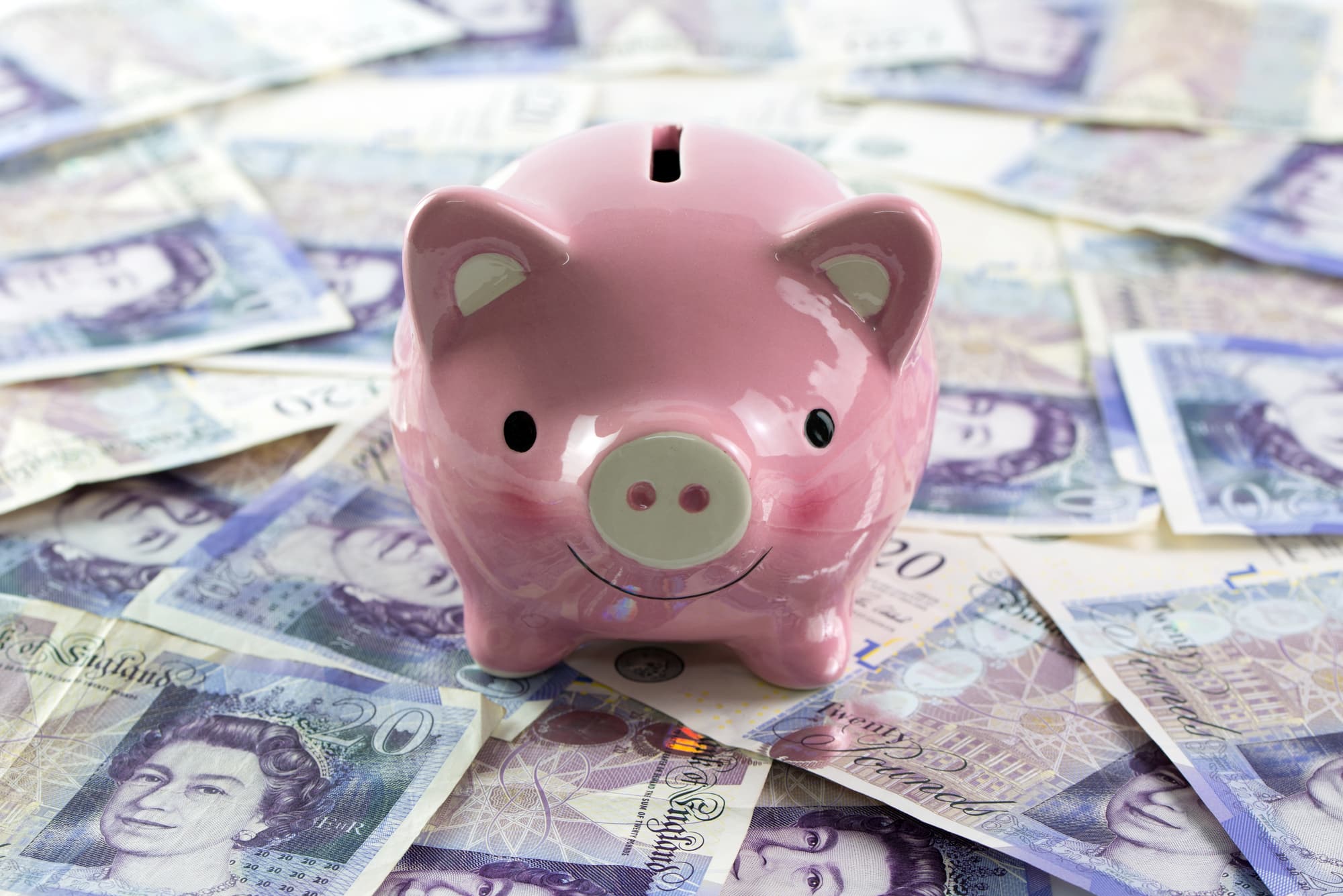 A pink piggy bank sits on a pile of twenty-pound British banknotes.